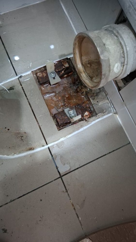 Brida del inodoro y pernos completamente oxidados bajo las baldosas